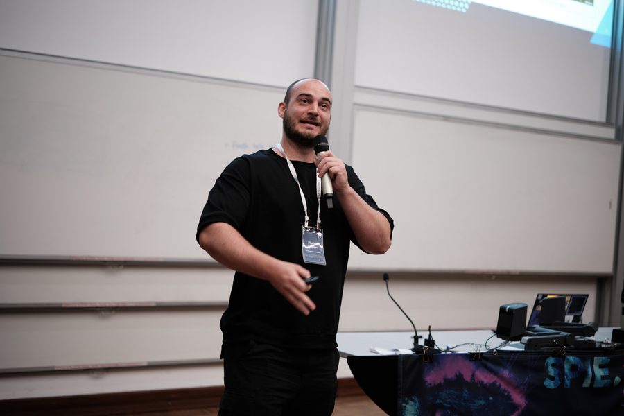 Dr Sulejman giving a conference talk, holding a microphone in front of a presentation screen